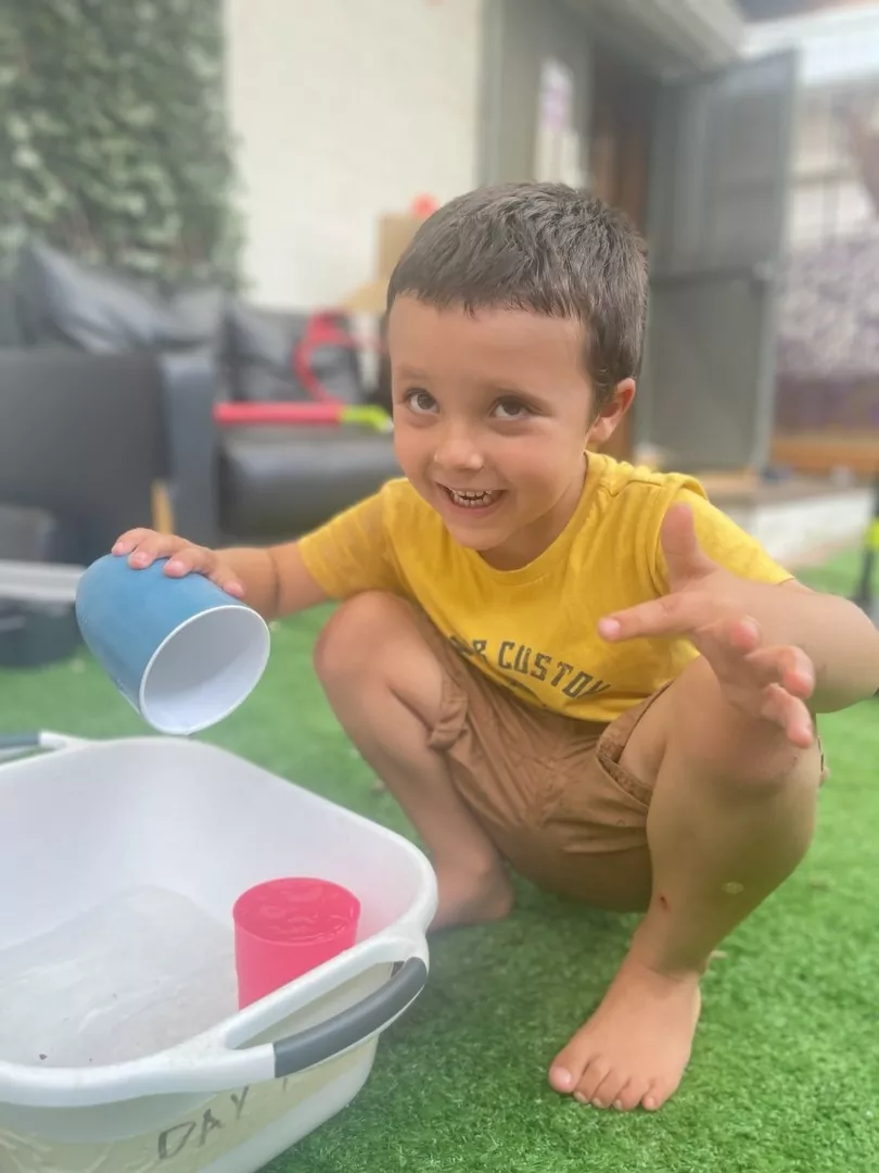 A young boy engaging in water play with a bucket of water.