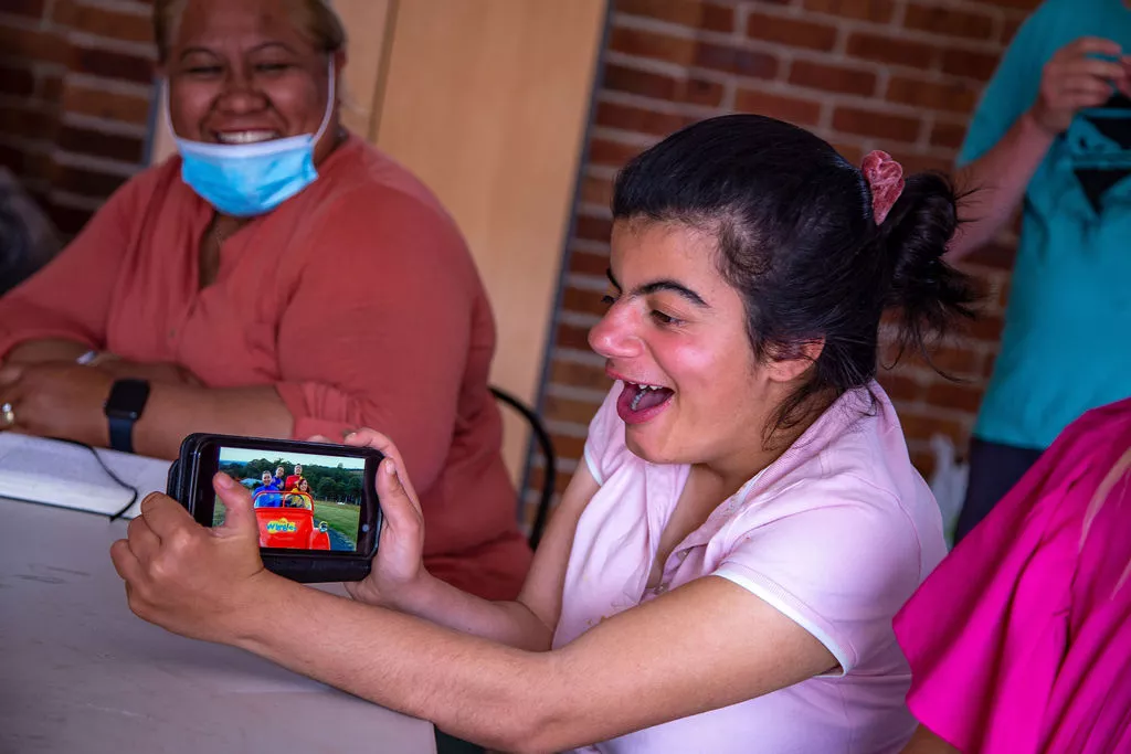 A group of people sitting around a table playing a game on a tablet as part of an NDIS activity.