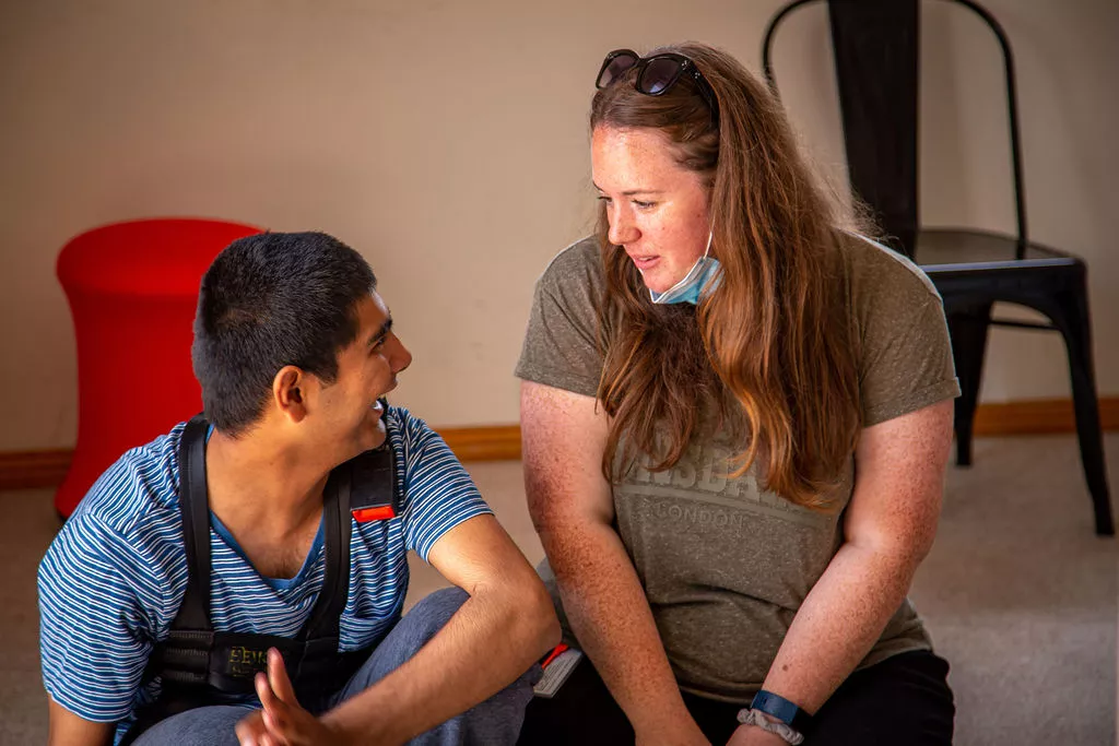 A man and woman engaged in a conversation on the floor, discussing NDIS.