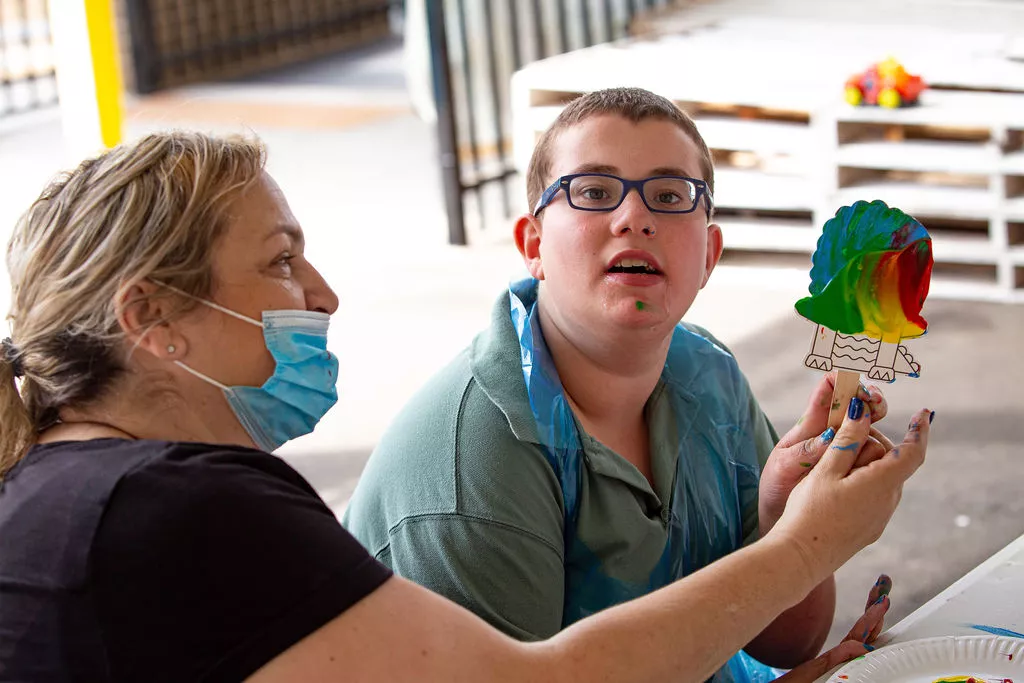 A woman wearing a face mask and a man holding a lollipop at an NDIS event.