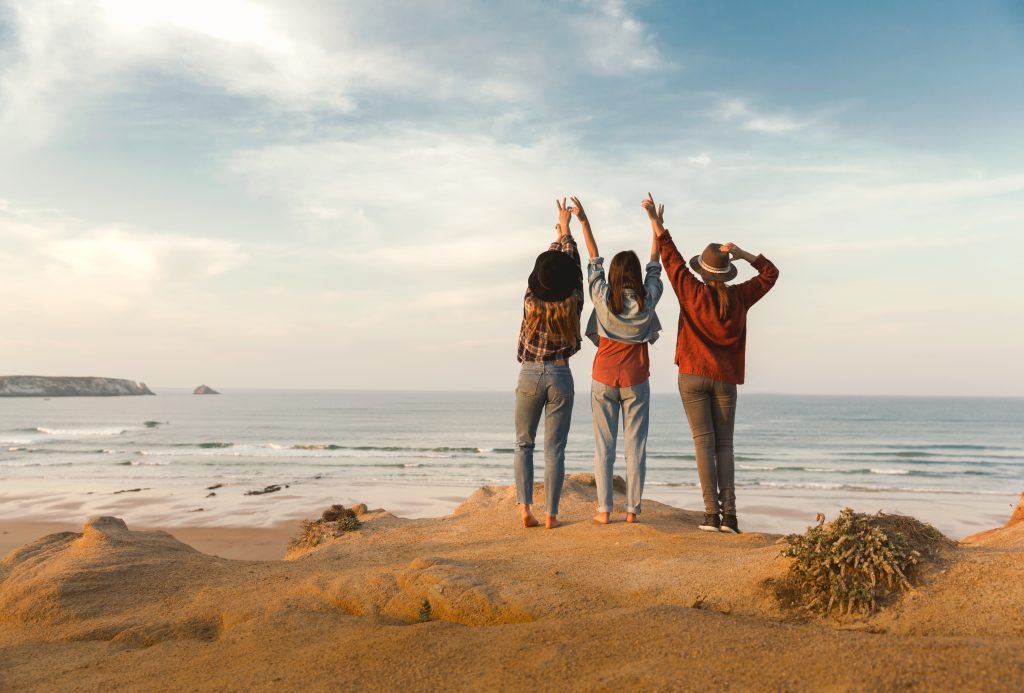 Three friends standing on a cliff overlooking the ocean embrace the breathtaking view.